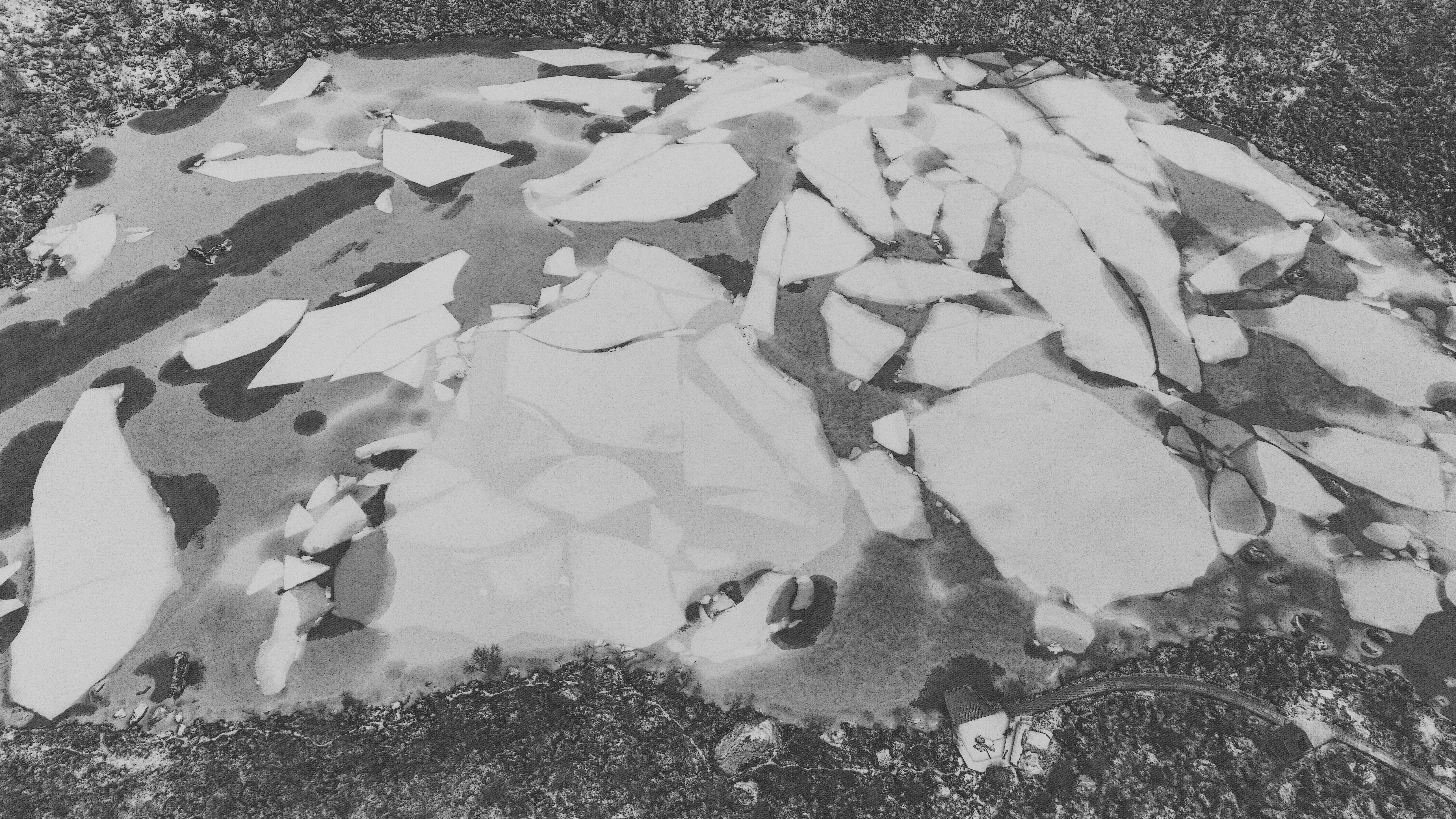 Composition graphite d’une photographie aérienne de Théophane Kiefer : les plaques d’un lac gelé au milieu d’une forêt enneigée.